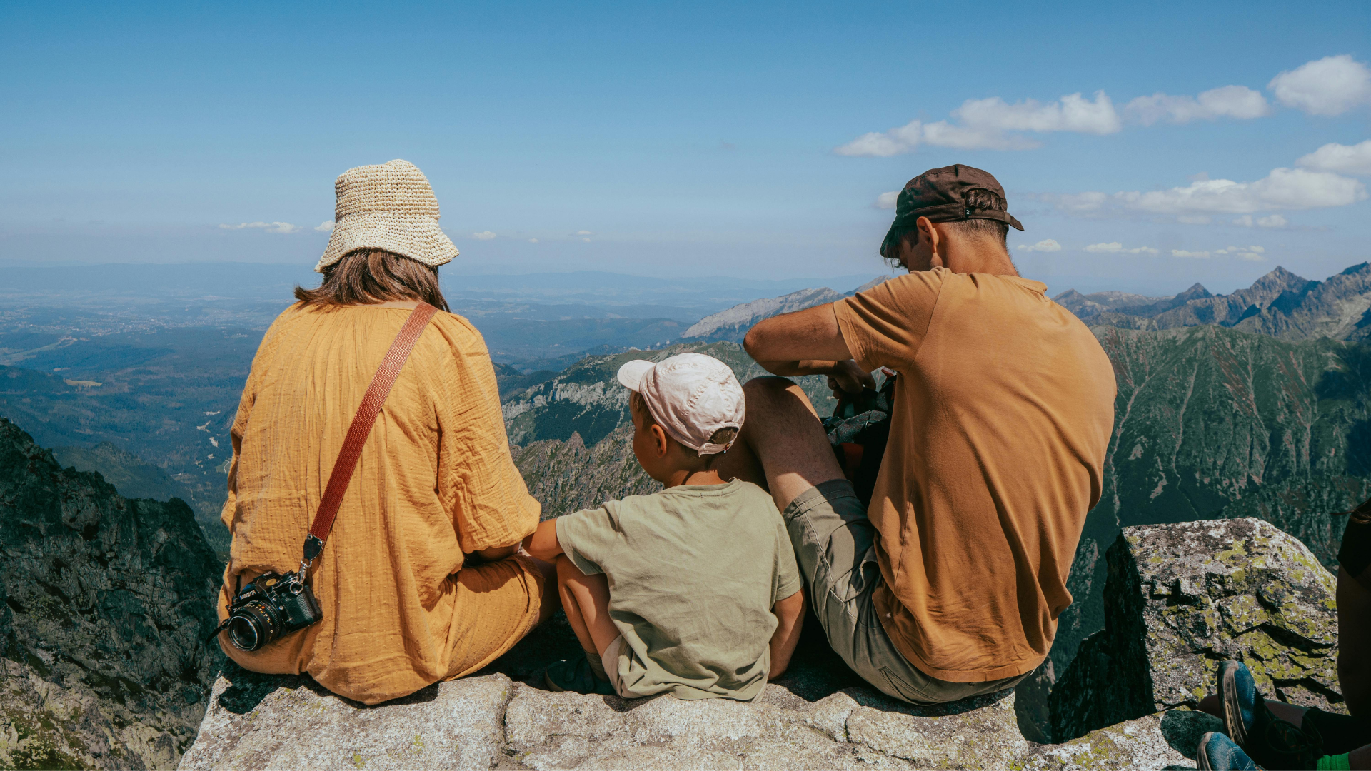 A family sitting together on a mountain summit, looking out over a vast valley view.